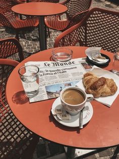 there is a cup of coffee and croissants on the table with newspaper