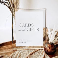 a card and gifts sign sitting on top of a table next to some dried plants