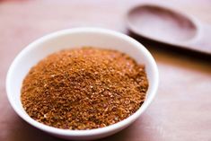 a white bowl filled with spices next to a spoon