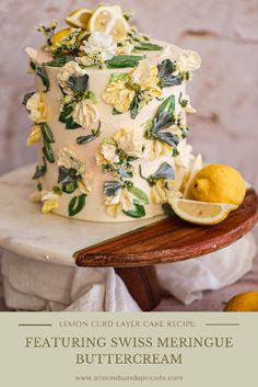 a white cake with yellow flowers and green leaves on top, sitting on a wooden platter