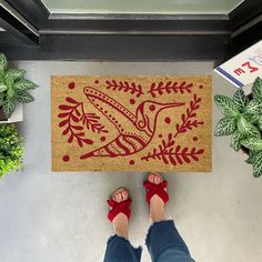 a person standing in front of a door mat with a bird on it and plants