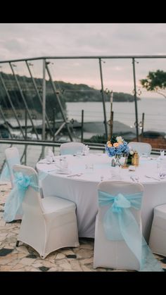 a table set up with white chairs and blue bows