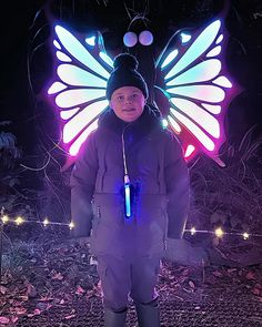 a young boy wearing a butterfly costume with lights on his head and wings, standing in the dark