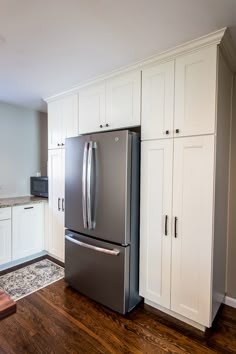 an empty kitchen with white cabinets and stainless steel refrigerator freezer combo in the center