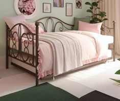 a bed with pink sheets and pillows in a room next to a potted plant