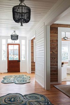 a hallway with wood paneling and white walls, two rugs on the floor and a chandelier hanging from the ceiling