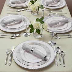 the table is set with silverware and white roses