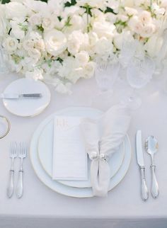 the table is set with white flowers and silverware