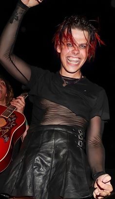 a woman with red hair and black leather skirt holding a guitar in her right hand