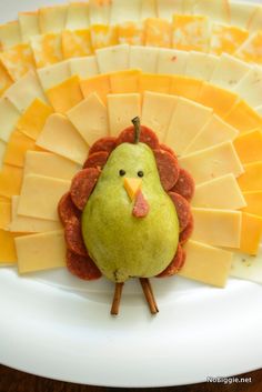 a white plate topped with cheese, fruit and a turkey shaped decoration on it's side