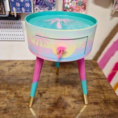 a pink and blue table with a palm tree painted on the top, sitting on a wooden surface