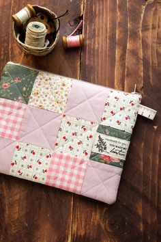 a pink and white patchwork purse sitting on top of a wooden table next to spools of thread