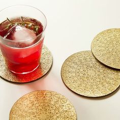 three coasters with gold leaf designs on them and a drink in a glass next to it