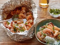 two bowls filled with shrimp and rice on top of a wooden table next to a beer