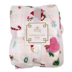 a white and pink plaid blanket with christmas decorations on it, sitting next to a tag that says royal standard luxury luxurious soft throw