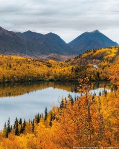 a lake surrounded by trees and mountains in the background with autumn foliage on it's sides