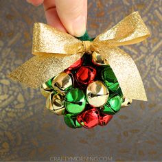 a hand holding a christmas ornament with bells on it and a bow around the top