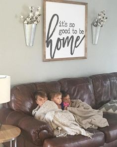 two children sitting on a brown couch in front of a sign that says it's so good to be home