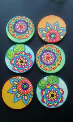 six colorful painted plates sitting on top of a black table next to an orange and blue flower