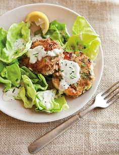 a white plate topped with lettuce and meat patties next to a fork