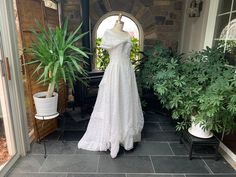 a wedding dress is on display in front of a doorway with potted plants and other greenery