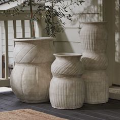 three white vases sitting on top of a wooden floor next to a planter