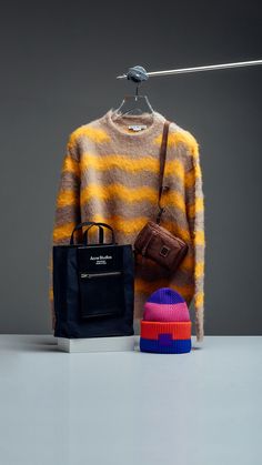 a sweater, bag and hat are sitting on a table in front of a gray background