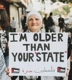 a woman holding a sign that says i'm older than your state in arabic