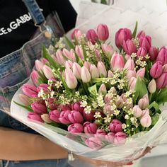 a person holding a bouquet of pink tulips and baby's breath flowers