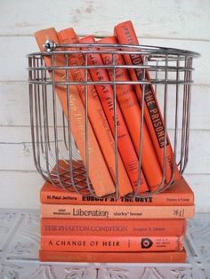 several books are stacked in a metal basket on top of each other, with orange covers