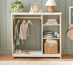 a white shelf with clothes and shoes on it in front of a green painted wall