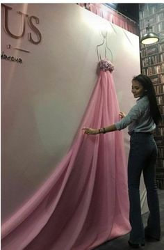 a woman standing next to a pink dress hanging on a wall in front of a sign