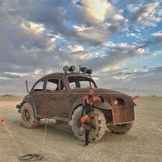 a woman sitting on top of an old car in the middle of a dirt field