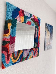 a multicolored mirror hanging on the side of a wall next to a window