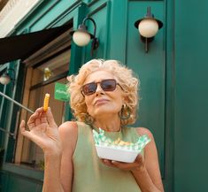 an older woman in sunglasses holding a box of food and looking up at the sky