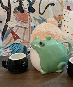 two tea cups and a frog mug sitting on a table