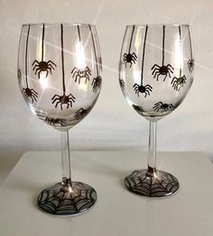 two wine glasses decorated with spider webs on white table top, side by side