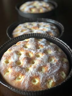 four pies are lined up on the table with powdered sugar covering them and sitting in pans