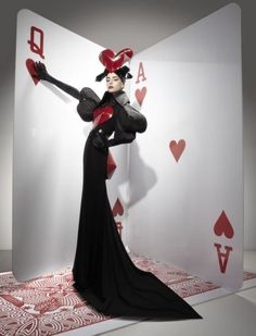 a woman dressed in black and red poses for the camera with her arms outstretched while holding cards