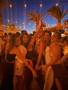 a group of women standing next to each other in front of palm trees at night