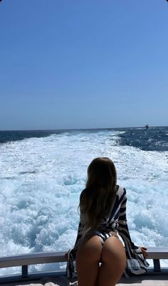 a woman sitting on the back of a boat looking out at the ocean and waves