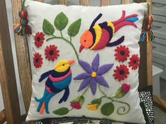 a decorative pillow on a chair with flowers and birds embroidered on the front, along with tassels