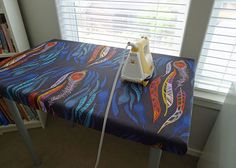 an ironing board on top of a table in front of a window with blinds