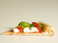 a piece of pizza with tomatoes, cheese and basil on it sitting on a white surface