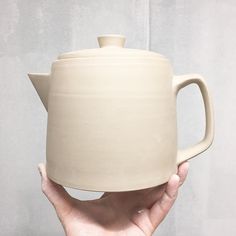 a hand holding a white ceramic tea pot