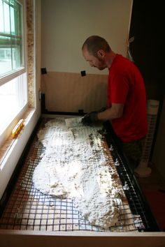 a man in red shirt and black gloves standing over a sheet of dough on top of a table