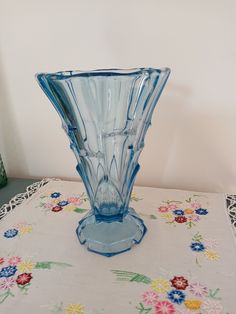 a blue vase sitting on top of a table next to a flowery table cloth