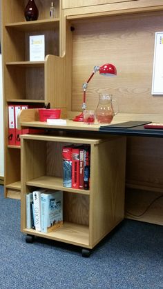 a wooden desk with books and a lamp on it in a room that has blue carpeting