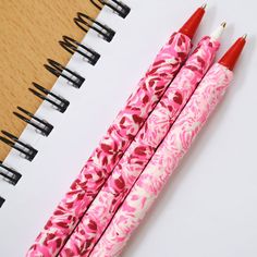 two pens sitting next to each other on top of a notebook covered in pink and white flowers