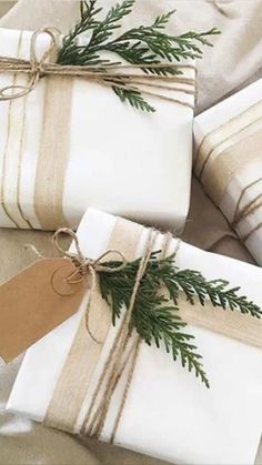 three wrapped presents tied with twine and decorated with pine needles, sitting on a bed